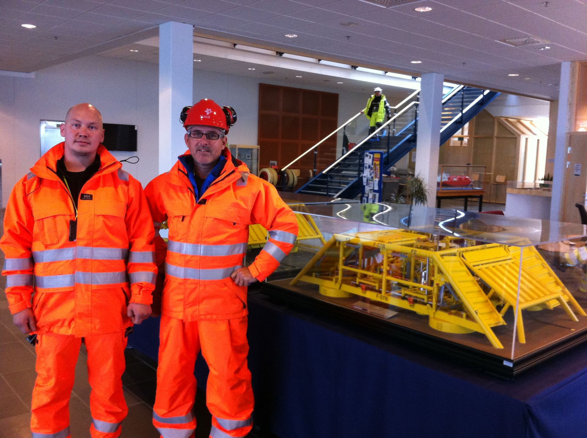Teknolog Roar Vigre og produksjonsleder ved ØB Hammerfest, Jim Ronny Hansen, i synlighetstøy ved en modell av et subsea-anlegg