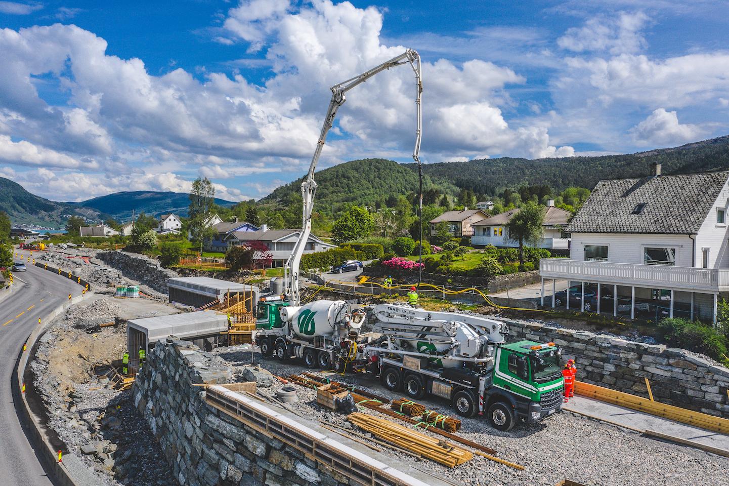 Two concrete trucks with pumps delivering concrete in Ølensvåg with a beatiful landscape background.